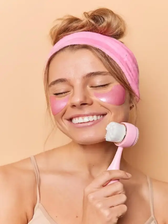 happy-healthy-woman-keeps-eyes-closed-applies-pink-hydrogel-patches-eyes-uses-face-massager-wears-he